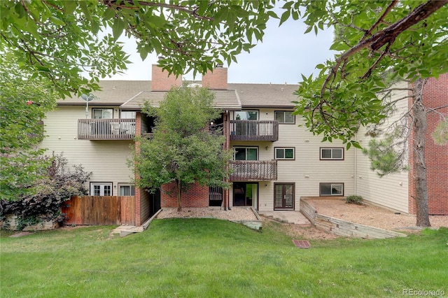 rear view of property featuring a balcony, a yard, fence, and a chimney