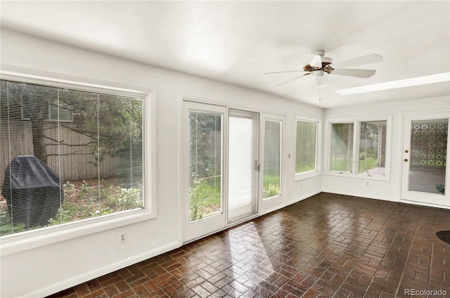 unfurnished sunroom featuring ceiling fan, a skylight, and plenty of natural light