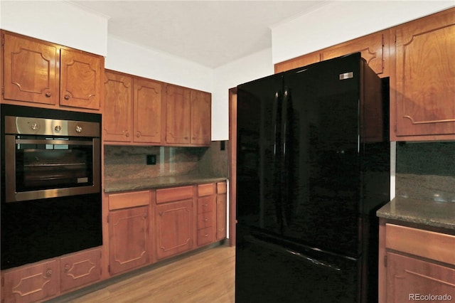 kitchen featuring black fridge, light hardwood / wood-style flooring, backsplash, crown molding, and stainless steel oven