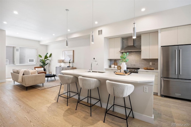 kitchen featuring wall chimney exhaust hood, a breakfast bar, a sink, and high end refrigerator