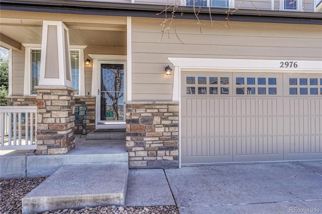 entrance to property with a garage, stone siding, and covered porch