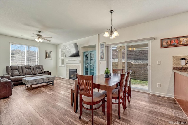 dining area featuring ceiling fan with notable chandelier, wood finished floors, a tiled fireplace, and visible vents