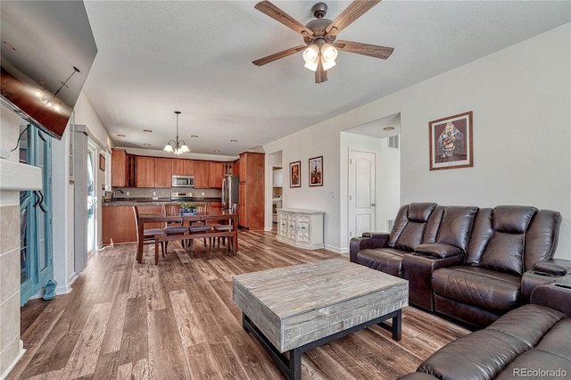 living area with visible vents, ceiling fan with notable chandelier, baseboards, and wood finished floors
