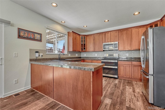 kitchen with a peninsula, visible vents, brown cabinetry, appliances with stainless steel finishes, and wood finished floors