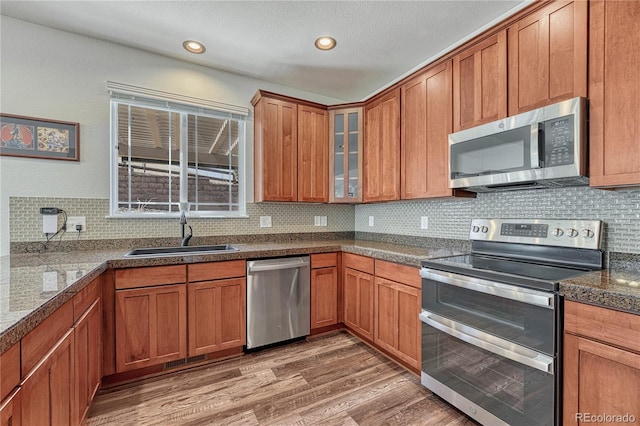 kitchen with glass insert cabinets, a sink, brown cabinets, stainless steel appliances, and light wood-style flooring