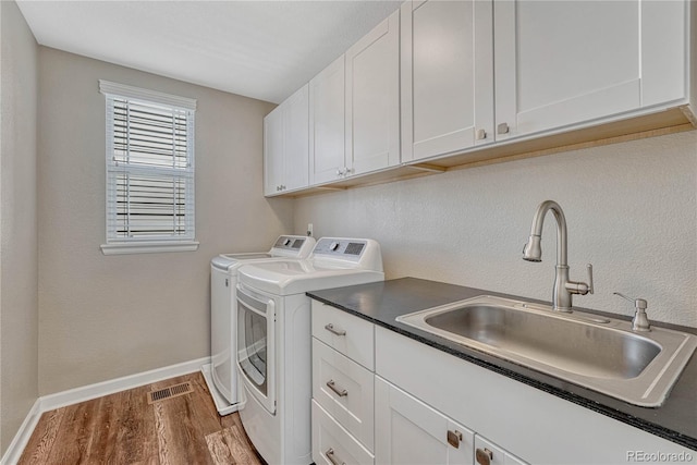 laundry room featuring wood finished floors, washing machine and dryer, a sink, baseboards, and cabinet space