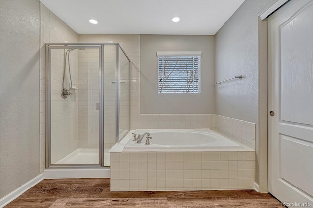full bath with a shower stall, a bath, wood finished floors, and a textured wall