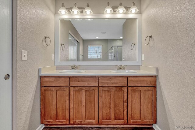bathroom with a stall shower, double vanity, a sink, and a textured wall