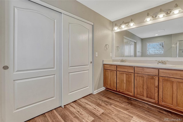 full bath featuring a shower with door, double vanity, a sink, and wood finished floors
