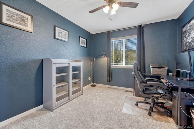 office area featuring a textured wall, carpet flooring, baseboards, and ceiling fan