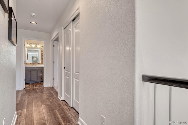 hallway with a sink, baseboards, a textured wall, and dark wood finished floors