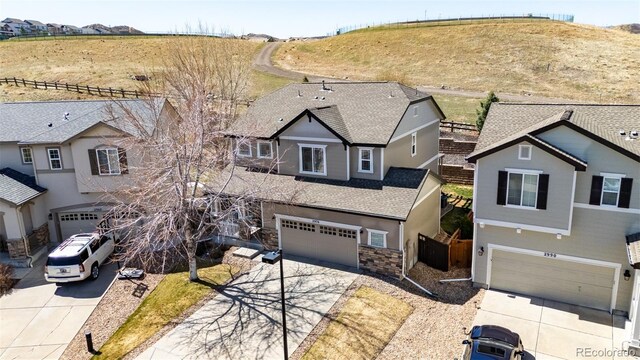 view of front facade featuring roof with shingles, stone siding, fence, an attached garage, and concrete driveway