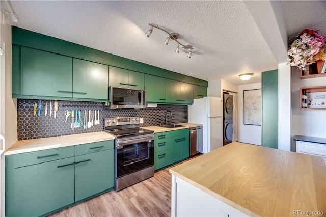 2917 S Locust St, Denver, CO 80222 - kitchen with appliances with stainless steel finishes, stacked washing machine and dryer, light wood-style floors, backsplash, and a textured ceiling