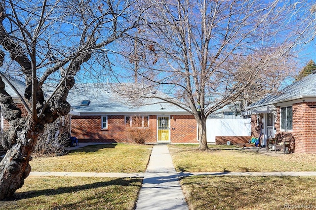 view of front facade featuring a shingled roof, fence, a front lawn, and brick siding