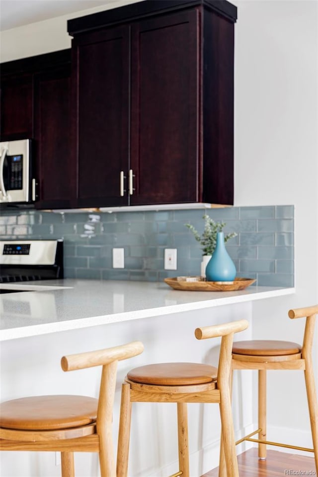 2931 W 20th Ave, Denver, CO 80211 - kitchen featuring white microwave, backsplash, stainless steel stove, light countertops, and a breakfast bar area