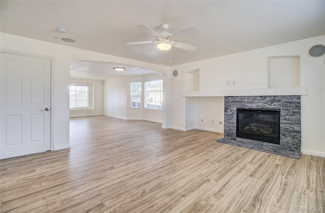 unfurnished living room with a stone fireplace, ceiling fan, and light hardwood / wood-style flooring