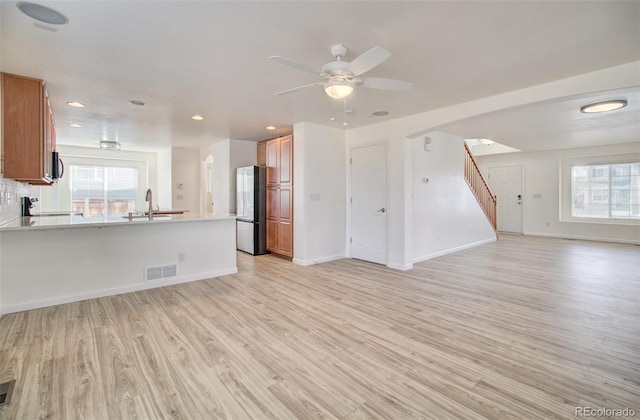 unfurnished living room with sink, ceiling fan, and light wood-type flooring