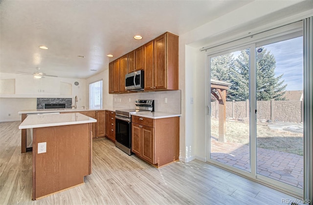 kitchen featuring appliances with stainless steel finishes, kitchen peninsula, light wood-type flooring, and backsplash