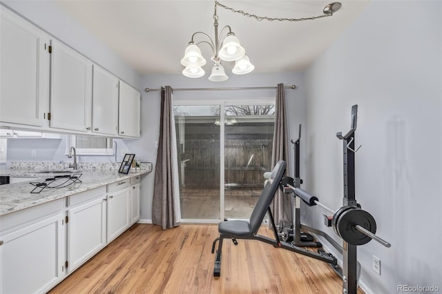 exercise room with a sink, a chandelier, baseboards, and light wood-style flooring