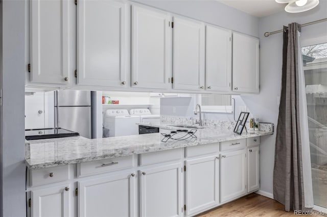 kitchen featuring light stone countertops, white cabinetry, freestanding refrigerator, a sink, and washer and dryer