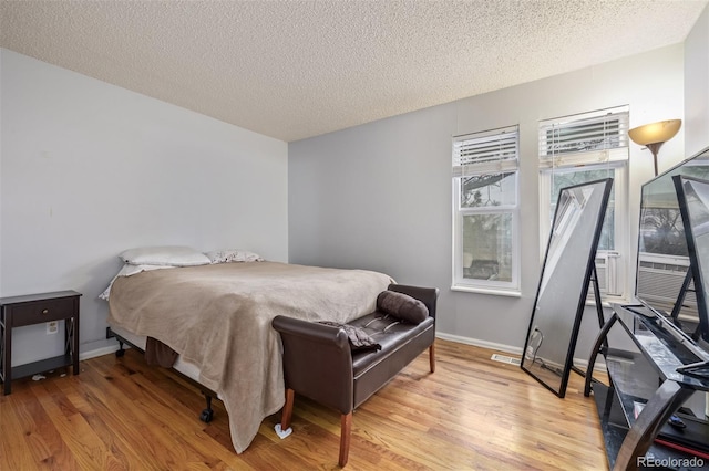 bedroom with light wood-type flooring, baseboards, and a textured ceiling