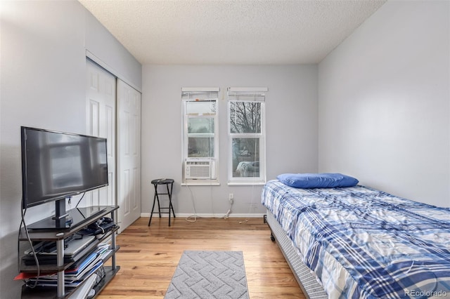 bedroom with cooling unit, baseboards, a textured ceiling, and light wood finished floors