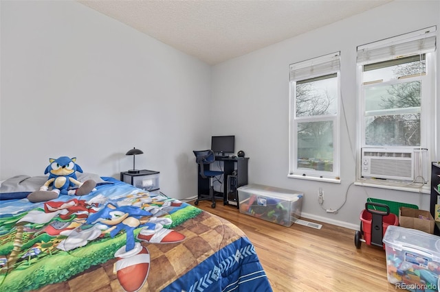 bedroom featuring visible vents, a textured ceiling, wood finished floors, cooling unit, and baseboards