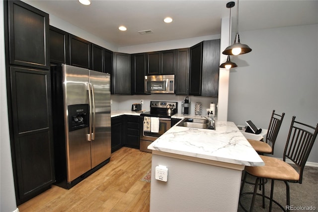 kitchen featuring a breakfast bar area, visible vents, hanging light fixtures, appliances with stainless steel finishes, and a sink