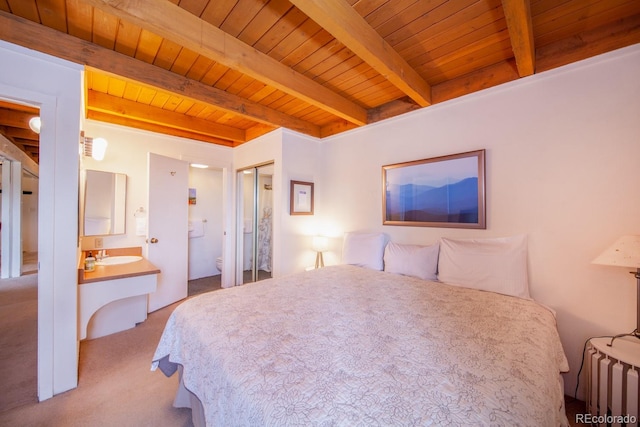 bedroom featuring beamed ceiling, wood ceiling, light colored carpet, and ensuite bath