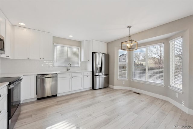 kitchen with pendant lighting, stainless steel appliances, light countertops, white cabinetry, and a sink