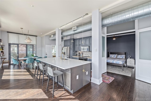 kitchen featuring a breakfast bar area, a center island with sink, dark wood-type flooring, light countertops, and stainless steel appliances