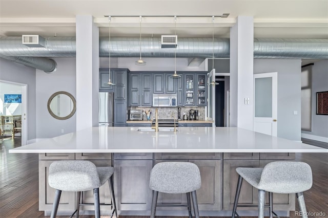 kitchen featuring appliances with stainless steel finishes, a sink, light countertops, dark wood finished floors, and a large island