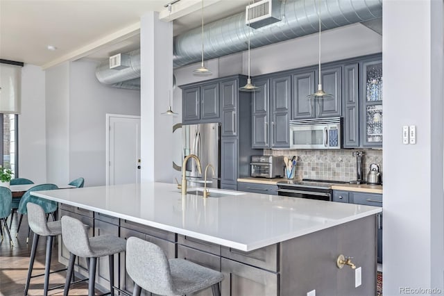 kitchen with appliances with stainless steel finishes, a breakfast bar, a sink, a kitchen island with sink, and tasteful backsplash