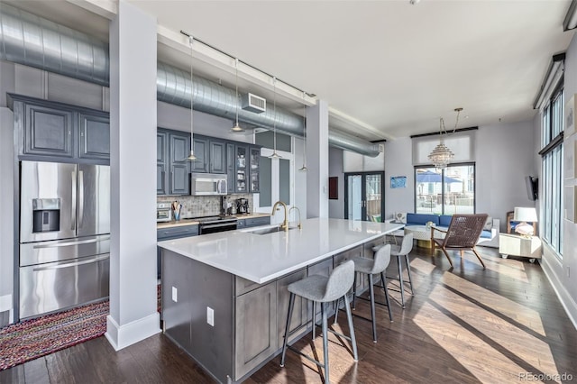 kitchen featuring decorative backsplash, a kitchen bar, appliances with stainless steel finishes, light countertops, and glass insert cabinets