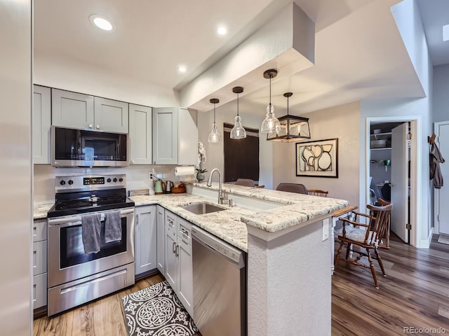 8680 Allison St Unit O, Arvada, CO 80005 - kitchen with stainless steel appliances, a peninsula, light stone counters, wood finished floors, and pendant lighting
