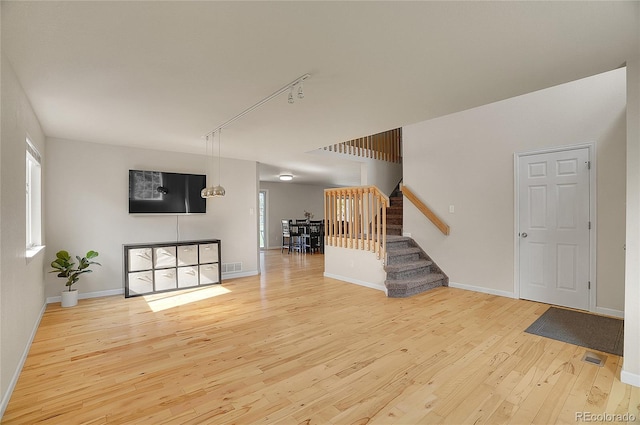 unfurnished living room featuring a wealth of natural light, visible vents, stairway, hardwood / wood-style floors, and baseboards