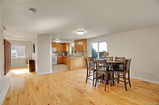 dining room with baseboards, a textured ceiling, visible vents, and light wood-style floors