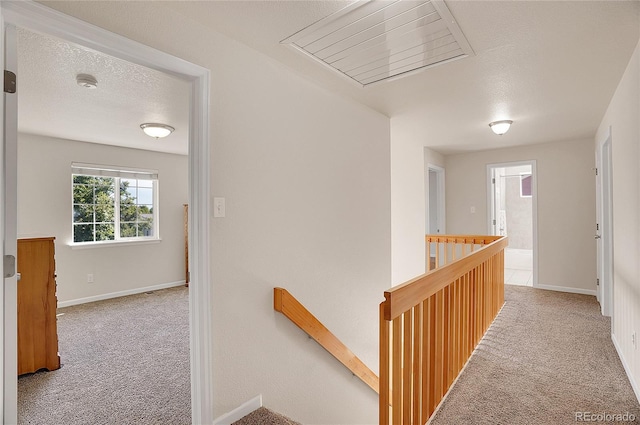 hallway featuring visible vents, baseboards, an upstairs landing, a textured ceiling, and carpet flooring