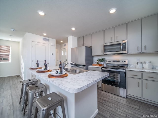 kitchen with hardwood / wood-style floors, a breakfast bar, stainless steel appliances, and an island with sink