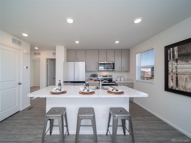 kitchen with a center island with sink, a kitchen breakfast bar, sink, gray cabinets, and stainless steel appliances