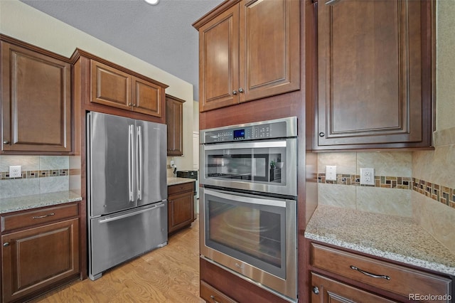 17670 W 94th Dr, Arvada, CO 80007 - kitchen featuring backsplash, light stone countertops, appliances with stainless steel finishes, and light wood-type flooring