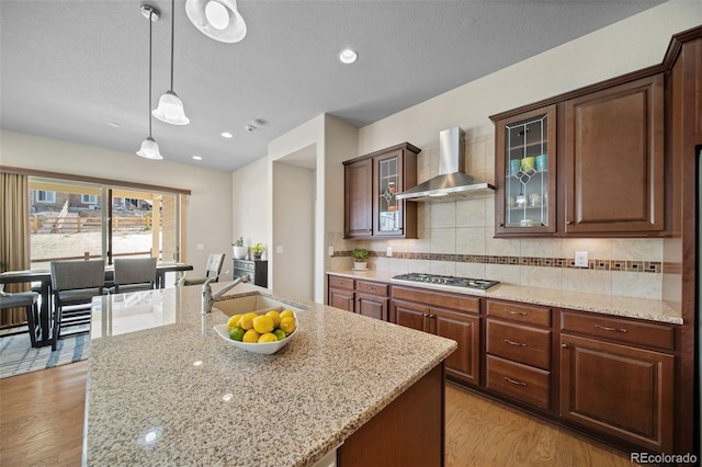 17670 W 94th Dr, Arvada, CO 80007 - kitchen featuring wall chimney range hood, stainless steel gas stovetop, backsplash, light stone countertops, and light wood-style floors