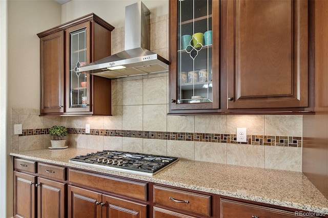 17670 W 94th Dr, Arvada, CO 80007 - kitchen with wall chimney range hood, decorative backsplash, stainless steel gas cooktop, light stone countertops, and glass insert cabinets