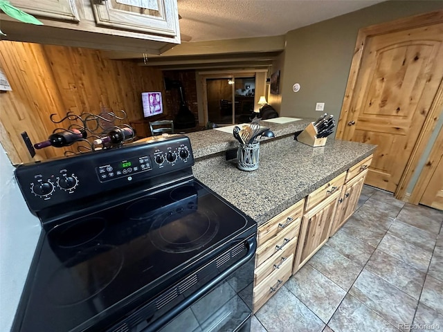 kitchen with light brown cabinetry, black range with electric cooktop, a textured ceiling, and wood walls