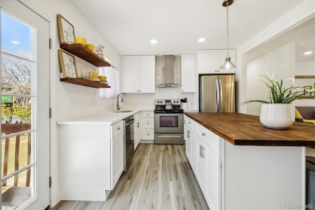 kitchen featuring appliances with stainless steel finishes, pendant lighting, butcher block countertops, sink, and wall chimney range hood