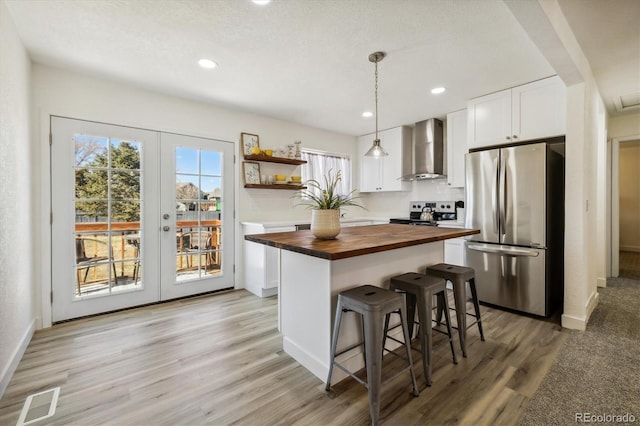 kitchen featuring wood counters, french doors, wall chimney exhaust hood, a center island, and stainless steel refrigerator