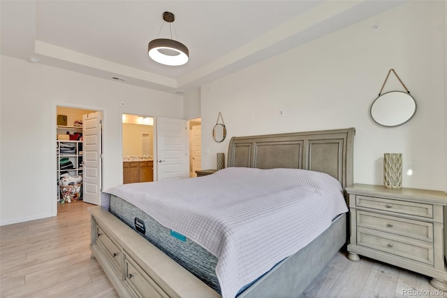 bedroom featuring light hardwood / wood-style floors, a raised ceiling, a walk in closet, and a closet