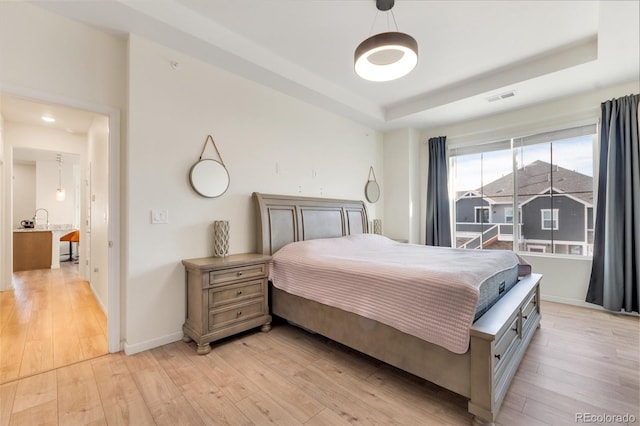 bedroom with light hardwood / wood-style floors and a raised ceiling