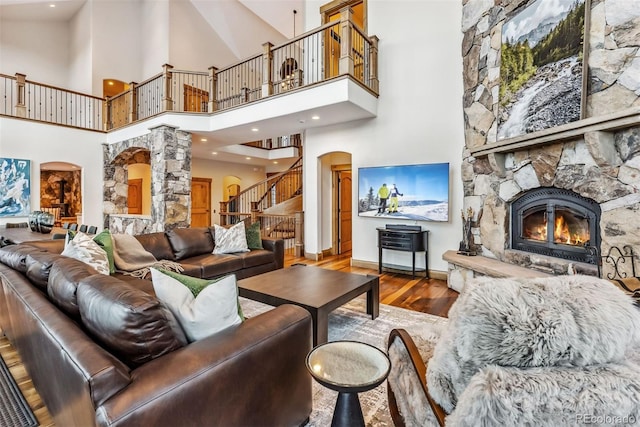 living room with hardwood / wood-style flooring, a towering ceiling, and a stone fireplace