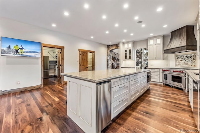 kitchen with light stone countertops, a center island, custom exhaust hood, white cabinetry, and double oven range